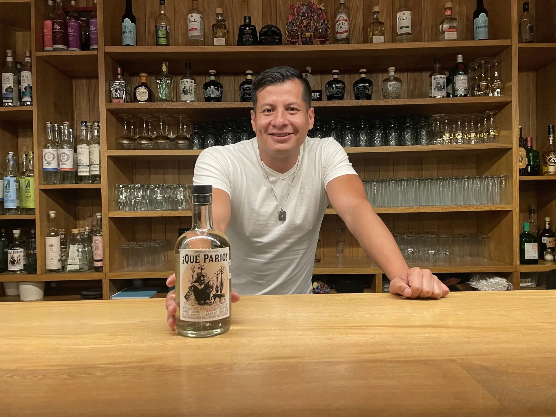 Sam with bottle of Que Pario behind bar